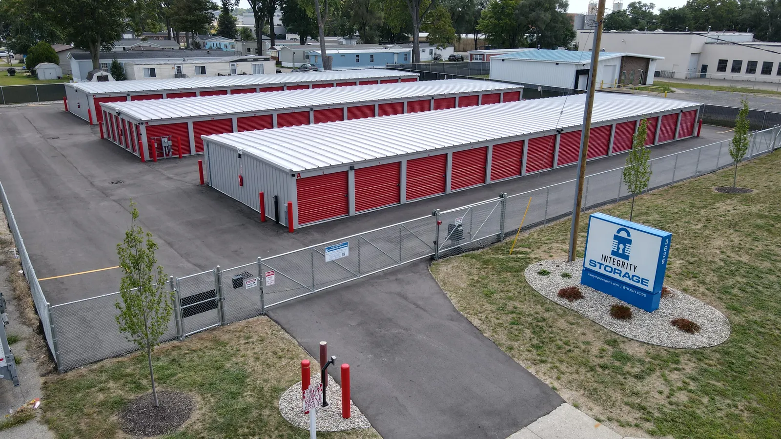 Aerial view of Integrity Storage: fenced lot with rows of red roll-up door units, keypad gate and blue Integrity Storage sign
